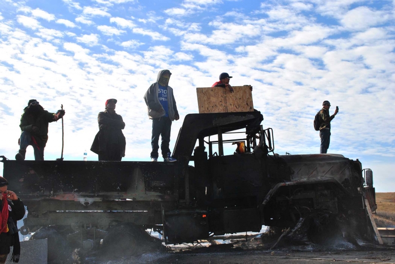 Activists on top of burned out DAPL machinery, fires still burning in gas tank - photo by C.S. Hagen